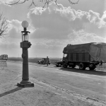Homme à côté de voitures et camions anciens sur une route rurale