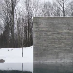 Mur en béton dans une forêt enneigée reflétant sur l'eau