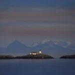 Phare et maison sur une île au crépuscule devant des montagnes