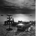 Voiture vintage et femme surplombant la mer au coucher du soleil