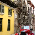 Voiture classique rouge dans une rue de ville avec échafaudages en bois