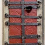 Porte en bois rouge renforcée de barres en métal noir et loquet