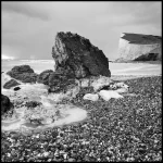 Plage rocheuse avec falaise dans un paysage côtier en noir et blanc