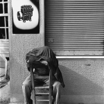 Homme assis caché sous un manteau devant une affiche "LISTEN"