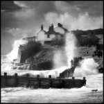 Maison sur une falaise au bord de mer avec vagues déferlantes en noir et blanc