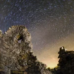 Ruine en pierres sous un ciel étoilé avec traînées de lumière