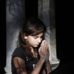 Jeune fille priant avec un chapelet en main