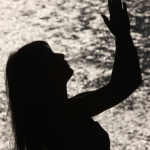 Silhouette d'une femme priant près d'une surface d'eau scintillante