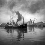 Navire dans un port industriel avec grues et fumée