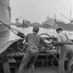 Docks industriels en activité avec deux ouvriers manipulant des cordages