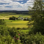 Vue panoramique d'un village européen entouré de champs et de collines sous un ciel nuageux