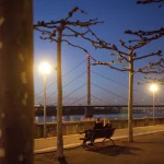 Couple assis sur un banc devant un pont illuminé au crépuscule