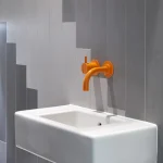 Évier blanc avec robinet orange sur un mur carrelé gris