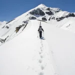 Alpiniste seul montant un sommet enneigé par temps ensoleillé