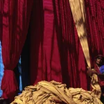 Femme manipulant des tissus colorés devant de grands rideaux rouges