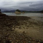 Plage rocheuse avec île et montagnes sous ciel nuageux