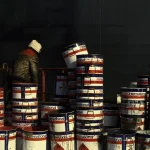 Personne travaillant dans une zone industrielle avec des barils de peinture empilés