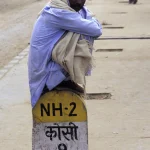 Homme assis sur borne kilométrique NH-2