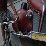 Enfant à Vélo à Côté d'une Voiture Ancienne