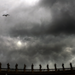 Statues surplombant une balustrade sous un ciel nuageux avec oiseau en vol