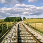 Chemin de fer longeant champs sous ciel nuageux