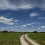 Chemin de terre sinueux sous un ciel bleu nuageux
