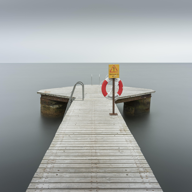 AKG8686944.webp Ponton en bois avec bouée de sauvetage sur une mer calme – Image 1