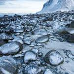 Roches enneigées sur la plage avec montagnes en arrière-plan