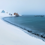 Village côtier enneigé avec maisons colorées et quai en ruine