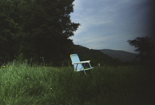 AKG8687011.webp Chaise bleue dans un pré verdoyant au crépuscule – Image 1