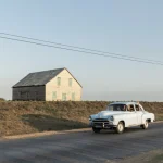 Voiture ancienne passant devant une maison en bois