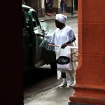 Femme en blanc ouvrant la porte d'une voiture verte dans une rue urbaine.