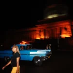 Femme marchant devant un vieux taxi bleu la nuit