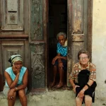 Trois femmes âgées assises devant une porte ancienne