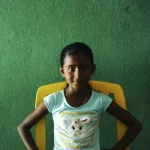 Jeune fille assise sur une chaise jaune devant un mur vert