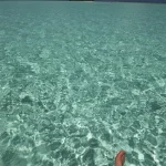 Pieds reposants dans une eau cristalline avec île à l'horizon
