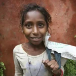 Jeune fille avec un sac en toile posant contre un mur rouge