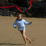Enfant courant avec un cerf-volant rouge sur la plage