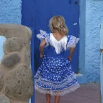 Petite fille en robe traditionnelle bleue devant une porte bleue