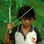 Enfant tenant une grande feuille dans une forêt dense.