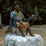 Homme en tenue colorée assis sur une chaise en extérieur tropical
