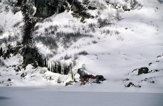 AKG884132.webp Chalet Rouge Enneigé au Pied d'une Montagne Rocailleuse – Image 1