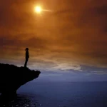 Personne seule au coucher du soleil sur une formation rocheuse surplombant la mer