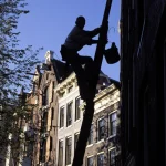 Nettoyeur de vitres montant une échelle en bois dans une rue urbaine