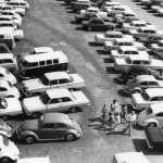 Parking rempli de voitures des années 1960 avec des gens marchant entre les véhicules