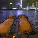 Barges de sable sur la rivière avec la ville illuminée en arrière-plan
