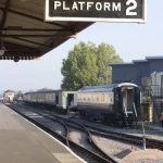 Gare ferroviaire avec panneau "Platform 2" et train sur les rails