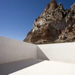 Mur blanc minimaliste face à une roche sur fond de ciel bleu