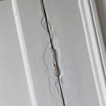 Charnière de porte endommagée montrant des fissures dans le bois