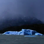Iceberg flottant devant des montagnes sous un ciel orageux
